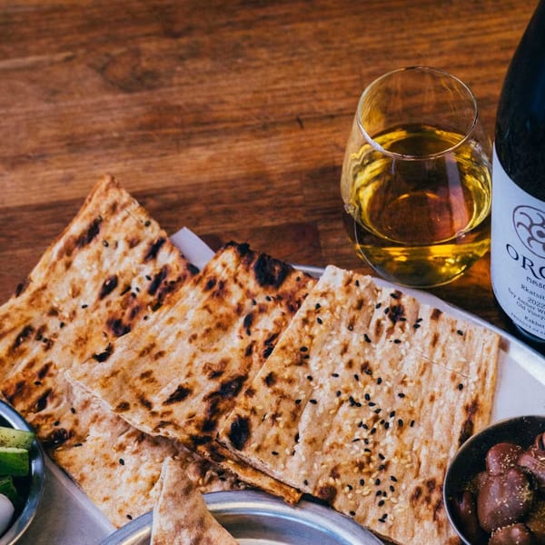 Flatbread, olives, pickled vegetables, and a glass of amber wine with a bottle of Orgo Rkatsiteli.