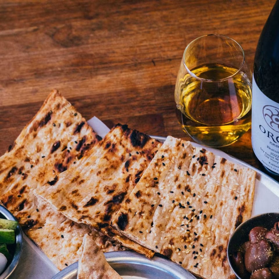 Flatbread, olives, pickled vegetables, and a glass of amber wine with a bottle of Orgo Rkatsiteli.
