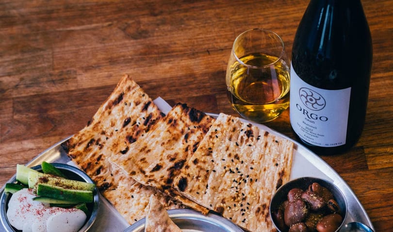 Flatbread, olives, pickled vegetables, and a glass of amber wine with a bottle of Orgo Rkatsiteli.