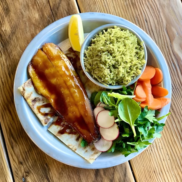 Glazed fish fillet with green rice, carrots, and a side salad with radishes and lemon.