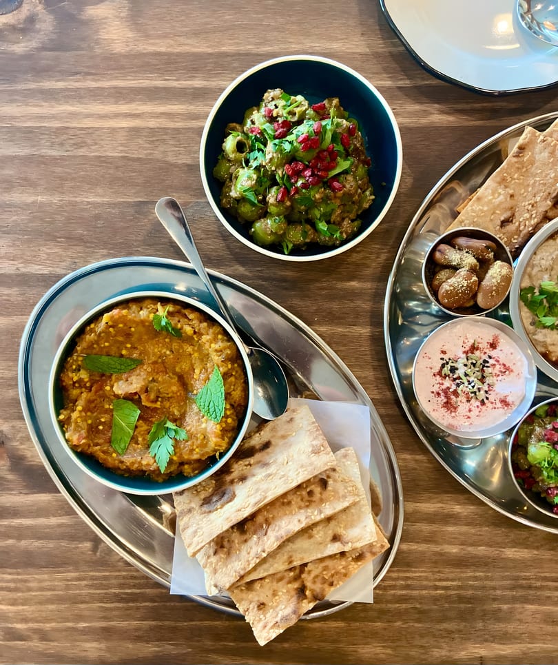 Overhead view of a mezze platter with dips, olives, and flatbread on a wooden table.