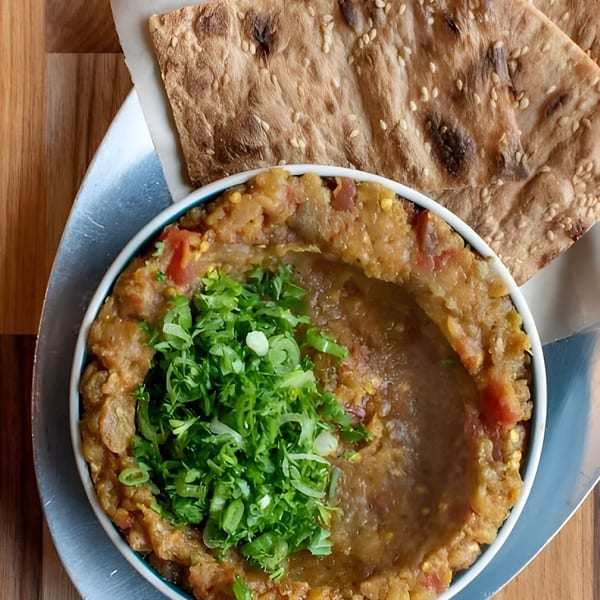 A bowl of mashed fava beans topped with green onions, served with sesame flatbread.