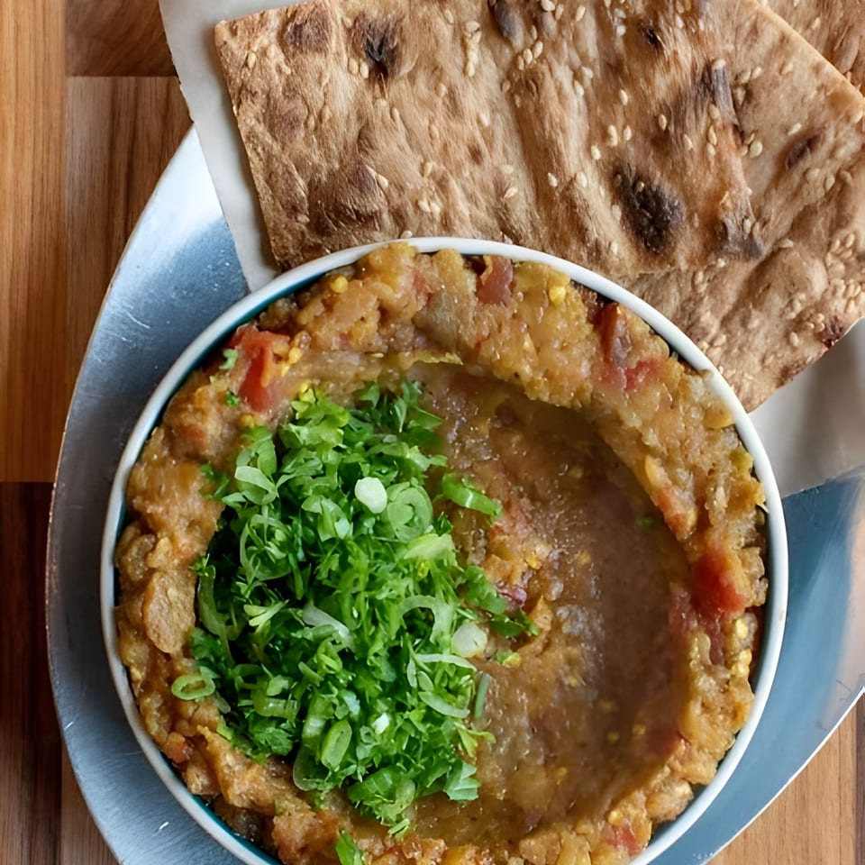 A bowl of mashed fava beans topped with green onions, served with sesame flatbread.