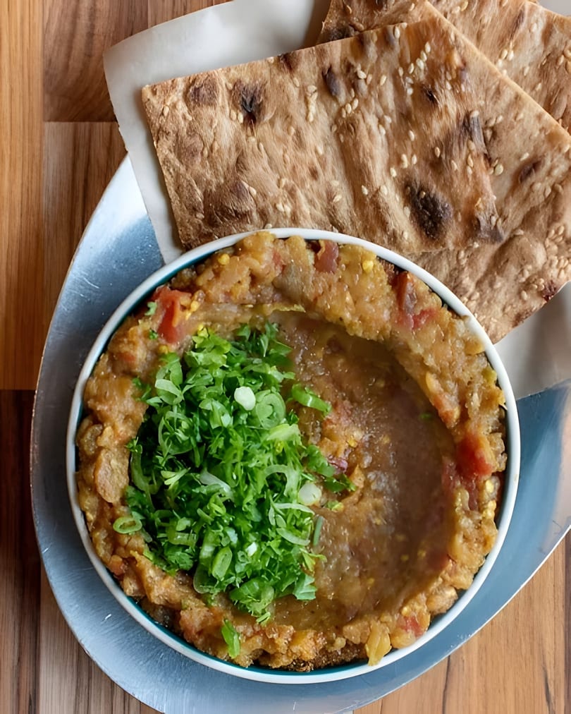 A bowl of mashed fava beans topped with green onions, served with sesame flatbread.