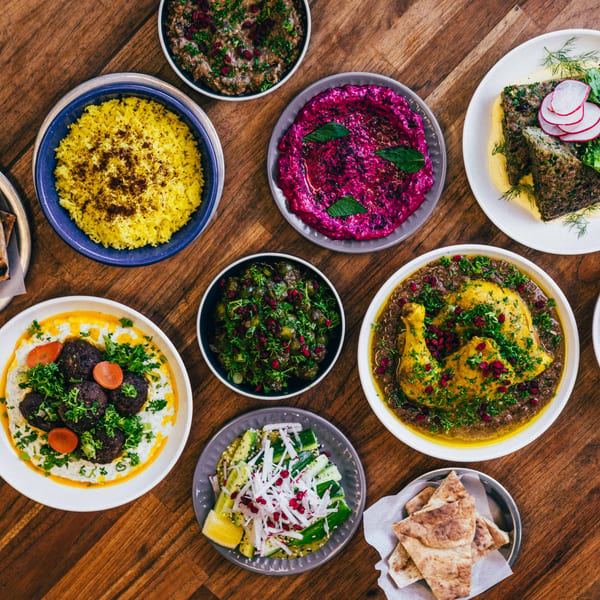 A top-down view of a wooden table laden with various colorful Middle Eastern dishes.