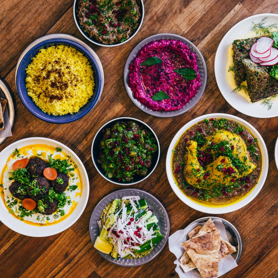A top-down view of a wooden table laden with various colorful Middle Eastern dishes.