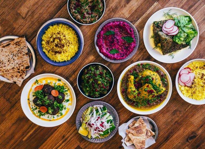 A top-down view of a wooden table laden with various colorful Middle Eastern dishes.