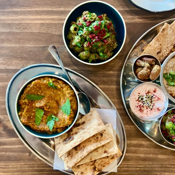 Overhead view of Middle Eastern dips, flatbread, and olives on two silver platters on a wooden table.