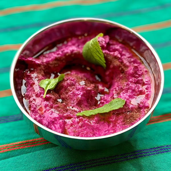 Vibrant pink beet hummus, drizzled with olive oil and garnished with fresh mint leaves in a silver bowl.