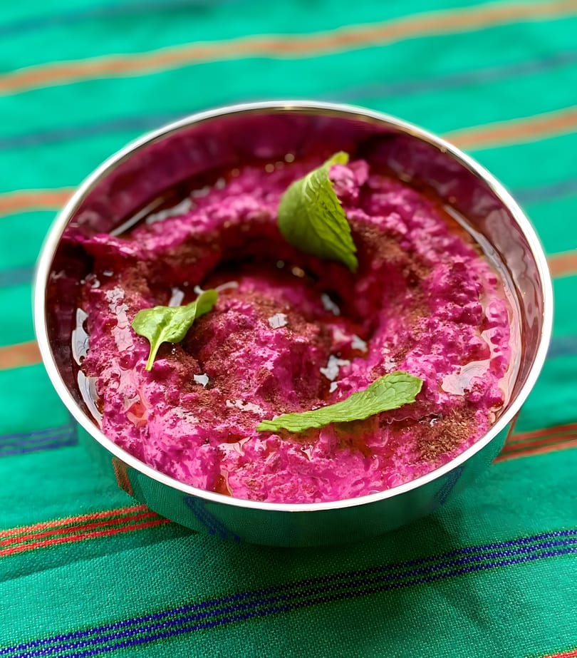 Vibrant pink beet hummus, drizzled with olive oil and garnished with fresh mint leaves in a silver bowl.