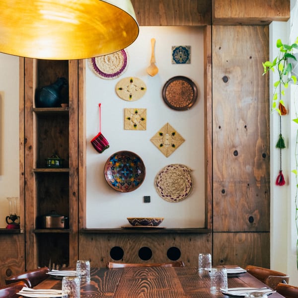 A long wooden dining table set with glasses and plates, under a large golden light fixture.