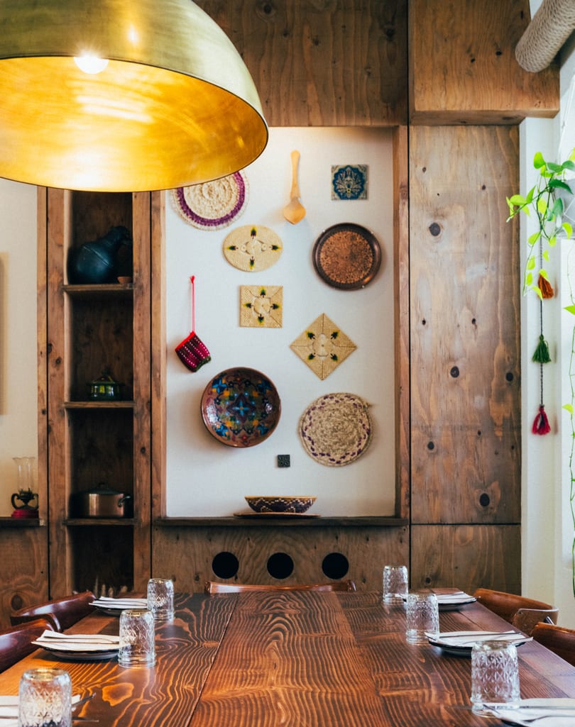 A long wooden dining table set with glasses and plates, under a large golden light fixture.