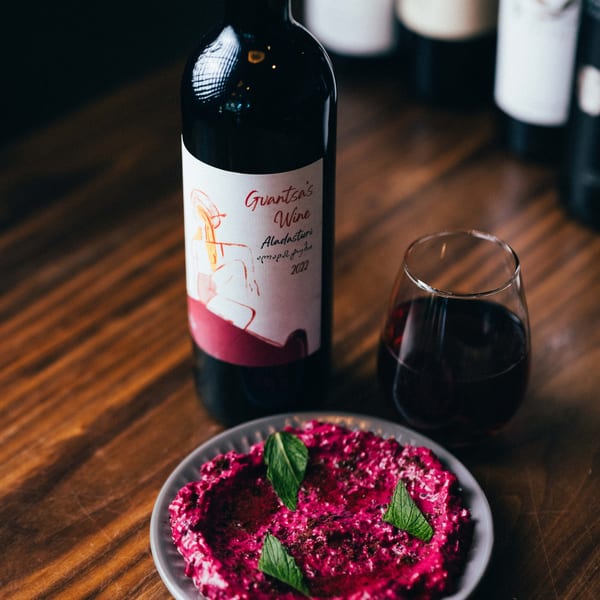 A bottle of red wine, a glass of red wine, and a plate of vibrant pink dip with mint.