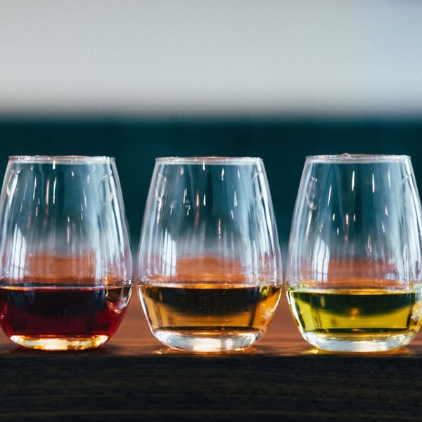 Five stemless wine glasses filled with different colored wines, from dark red to pale yellow.