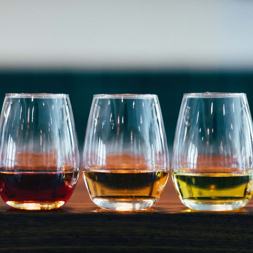 Five stemless wine glasses filled with different colored wines, from dark red to pale yellow.