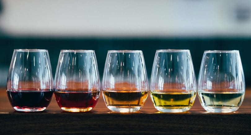 Five stemless wine glasses filled with different colored wines, from dark red to pale yellow.